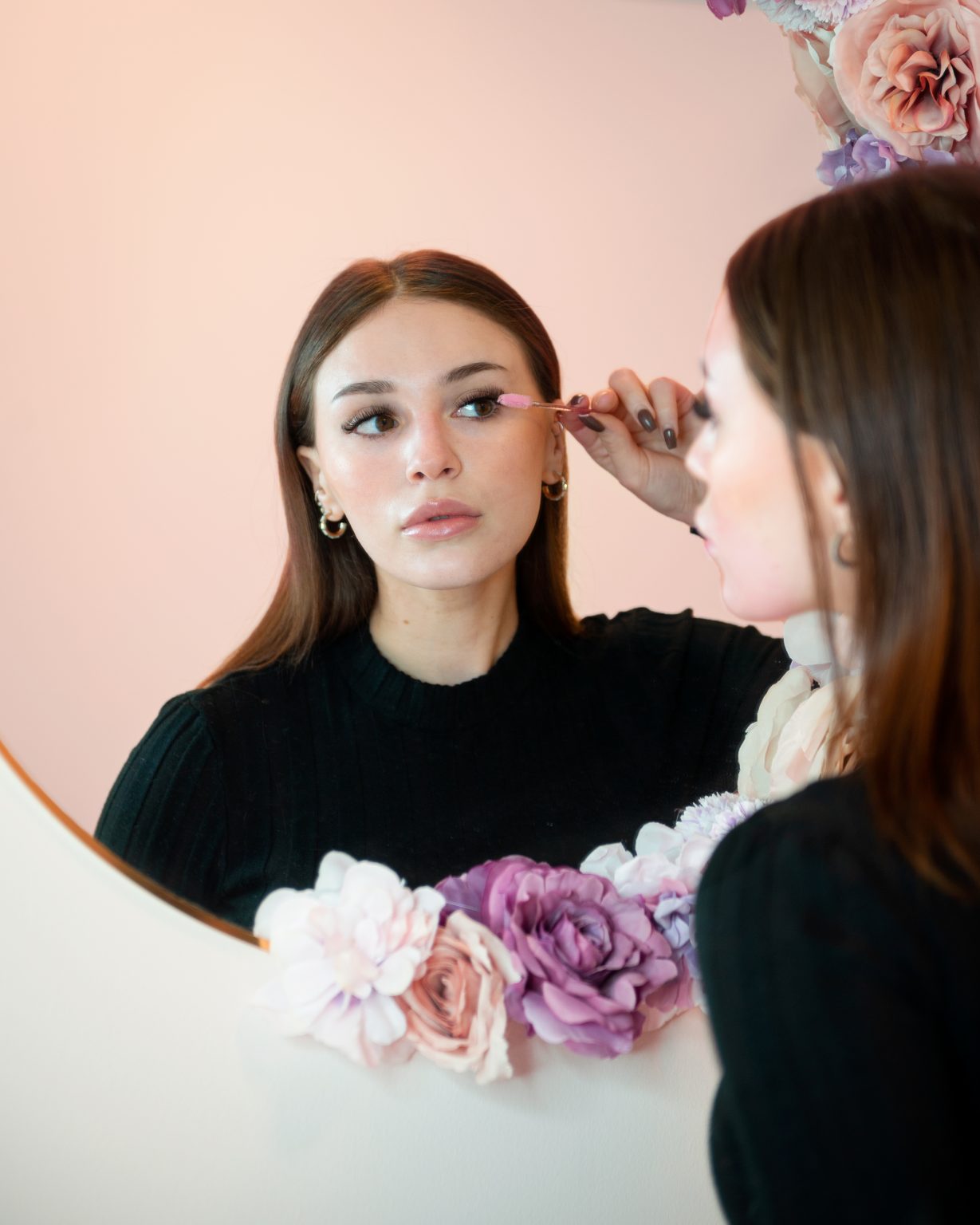 Kvinne i skjønnhetssalong som ser seg i speilet og børster øyevippene. Foto