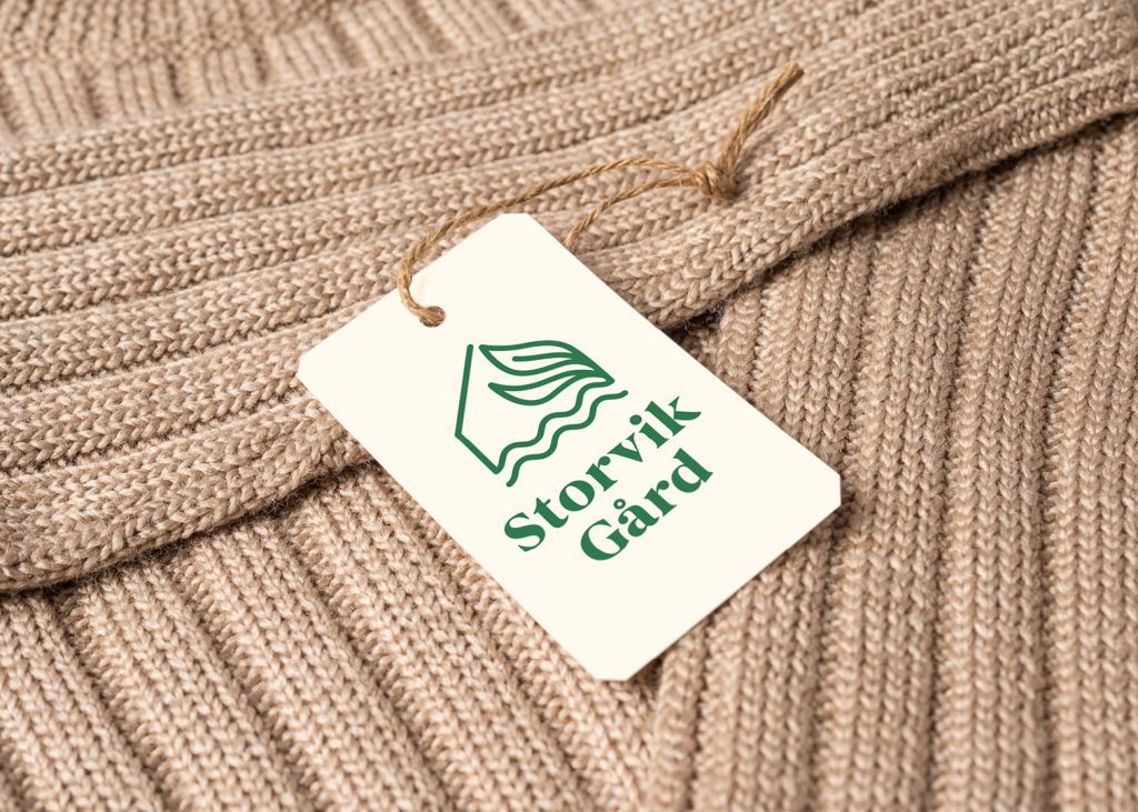 Storvik gård sin grønne logo på hvit etikett med strikkegenser i bakgrunnen. Bilde
